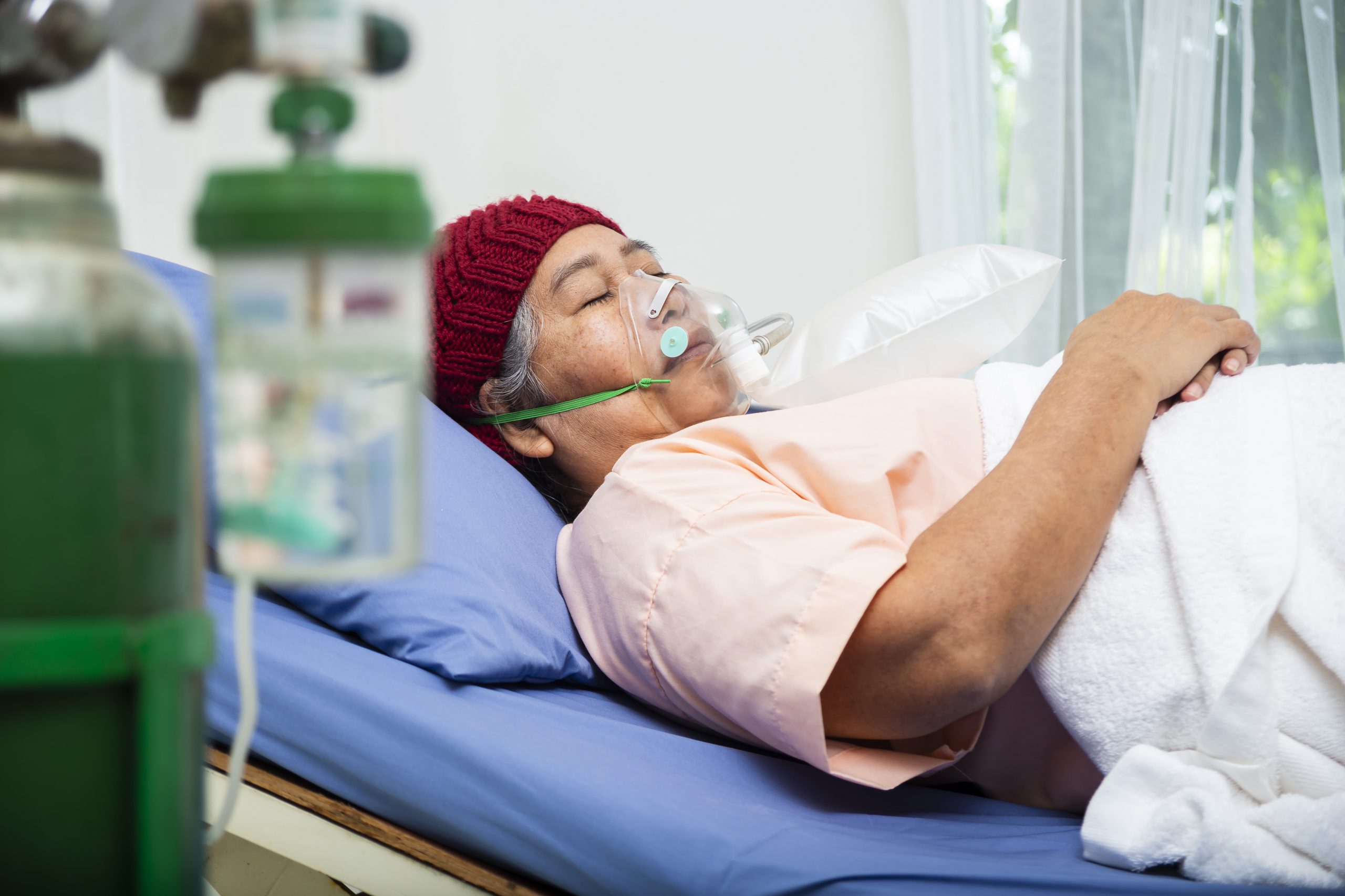 Asian elderly woman wearing wool hat with oxygen mask to breathing while  lying on patient bed, senior female medical and healthcare concept